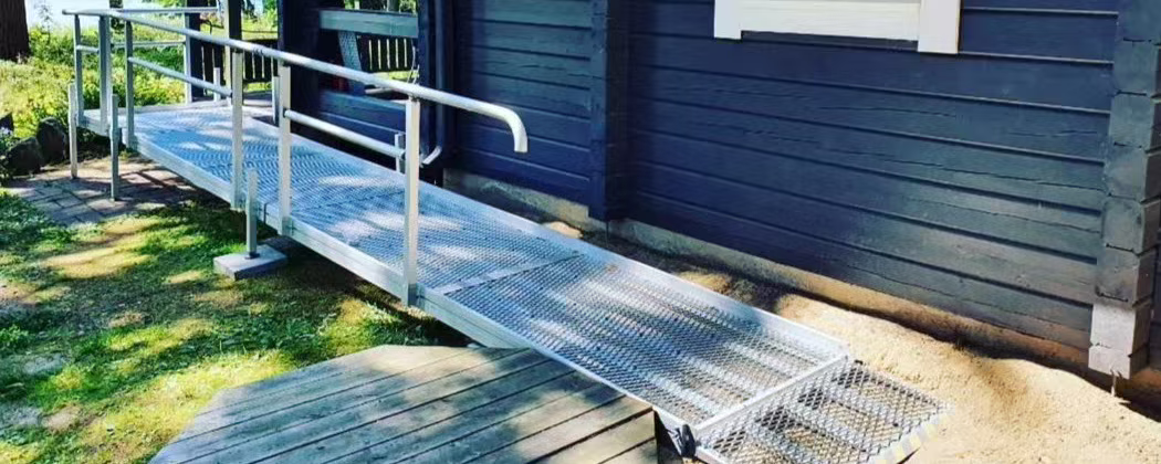 Metallinen pyörätuoliramppi kaiteineen hirsitalon sisäänkäynnillä