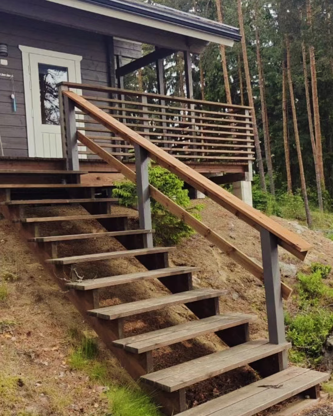 Puiset ulkoportaat ja pitkä tukikaide rinteessä