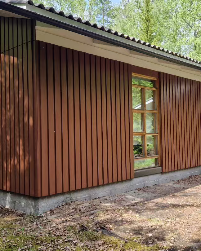Punaruskeaksi maalattu puinen piharakennus metsän reunassa